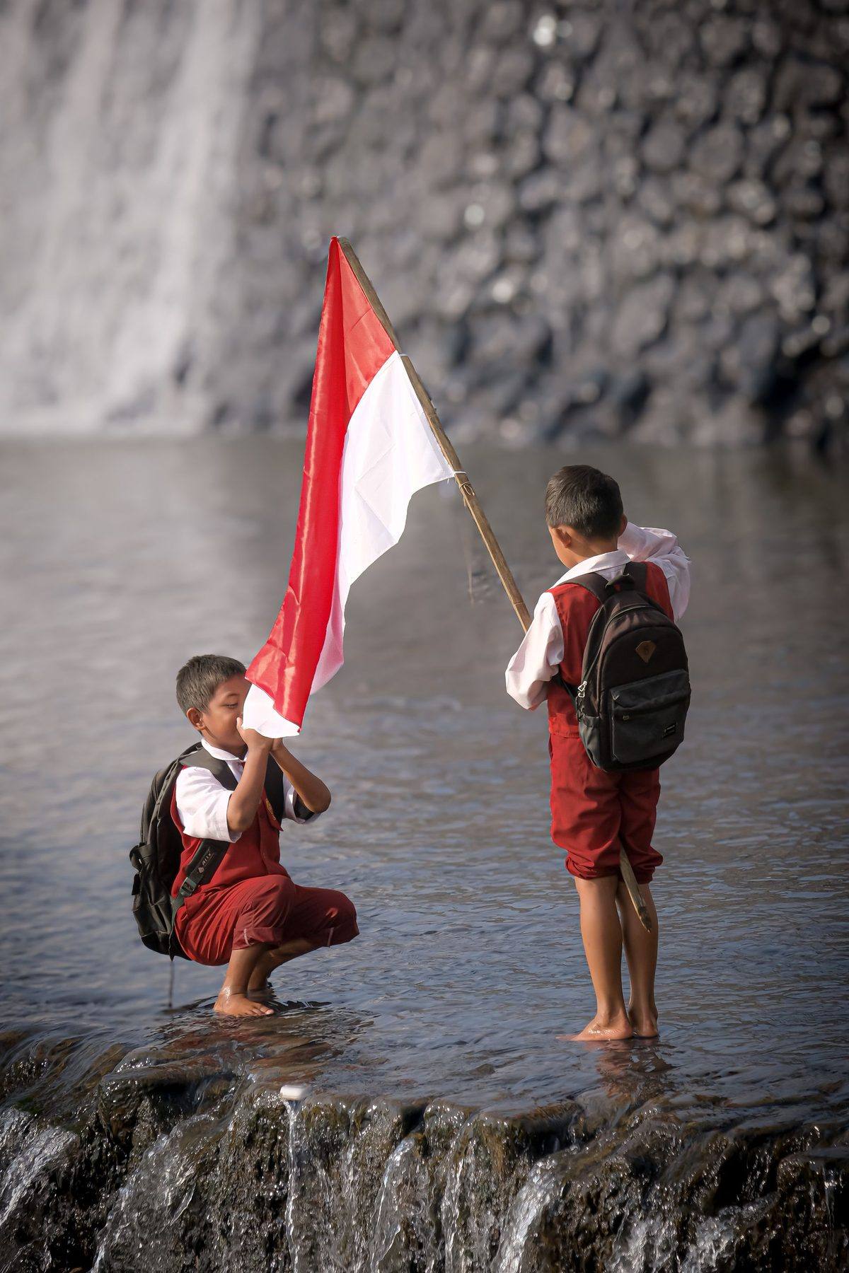 Dua siswa SD membawa bendera Merah Putih di tepi air