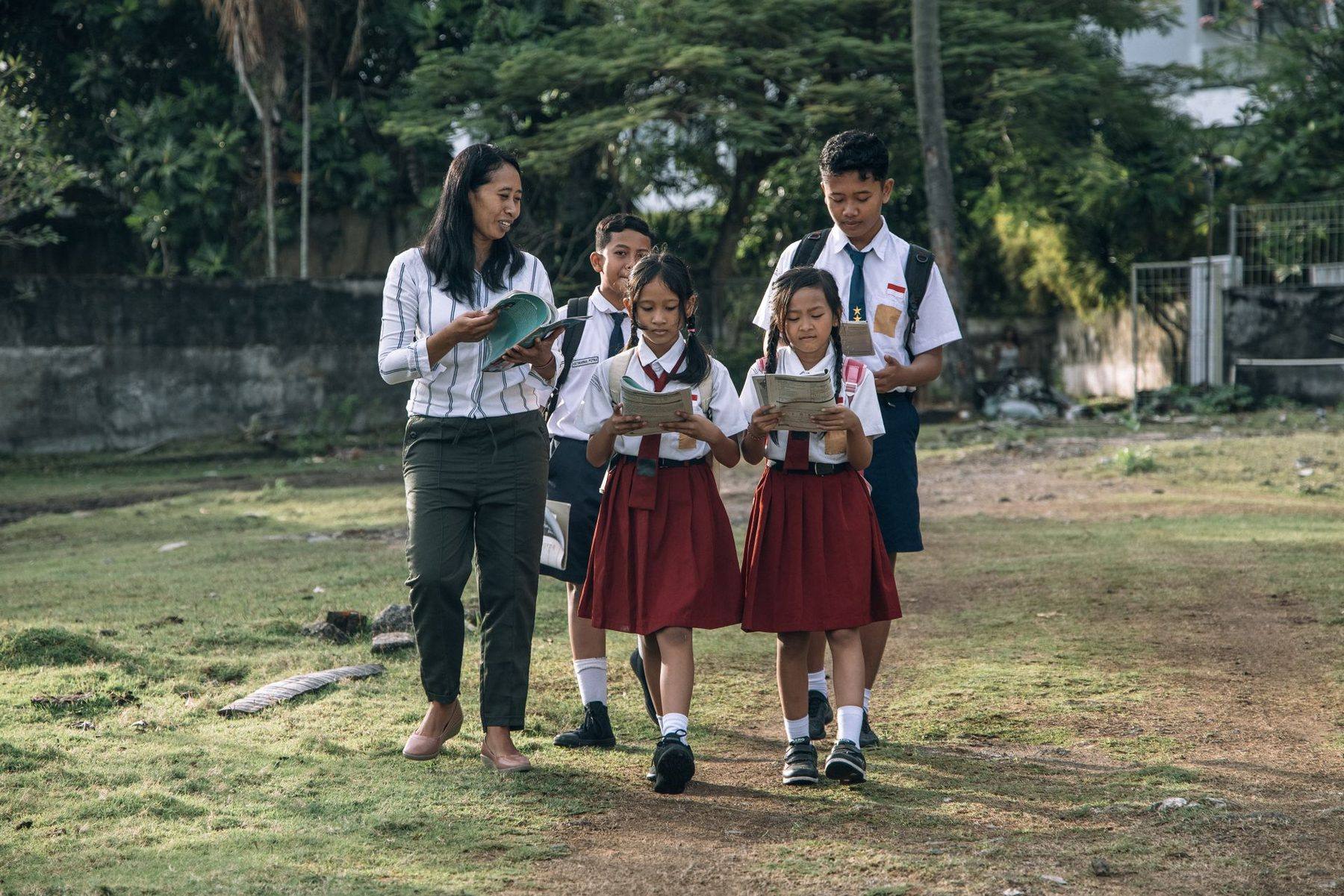 Guru berjalan bersama siswa berseragam sambil membawa buku