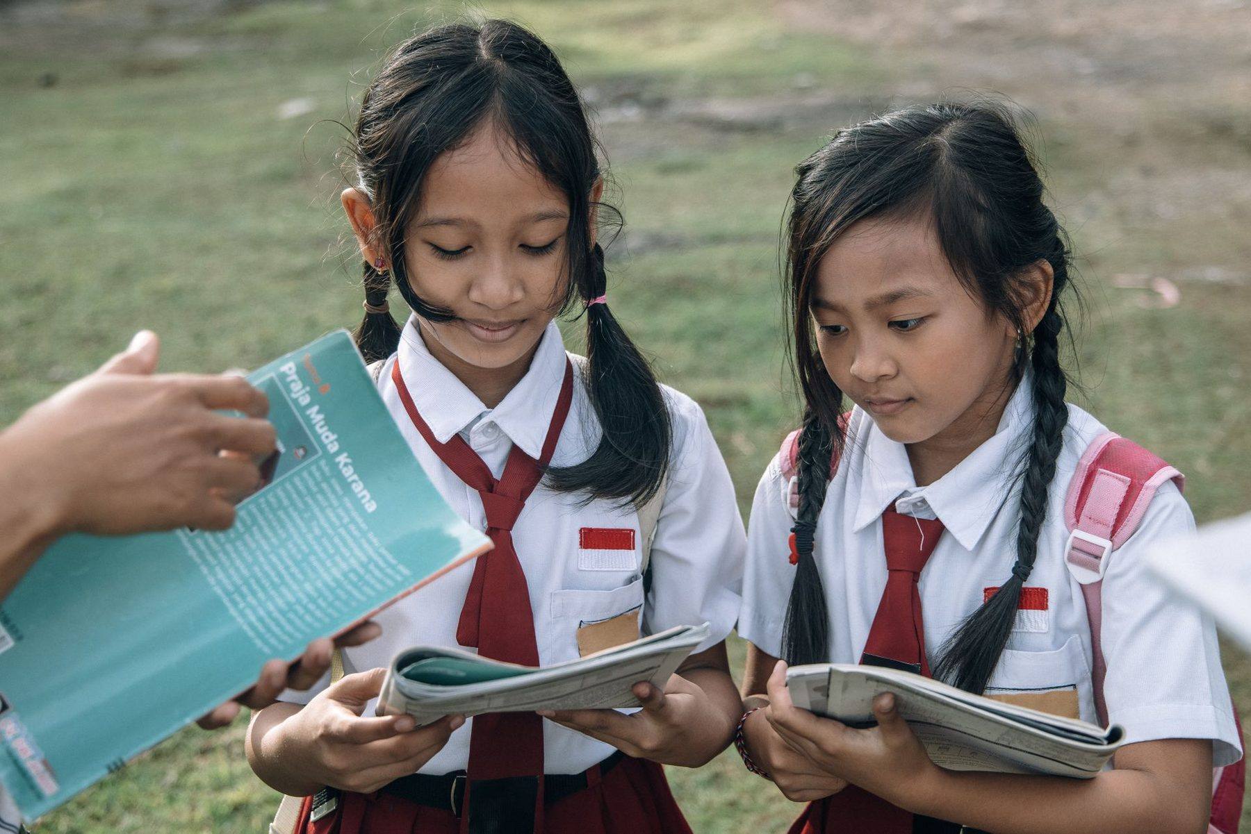 Dua siswi SD berkepang membaca buku pelajaran