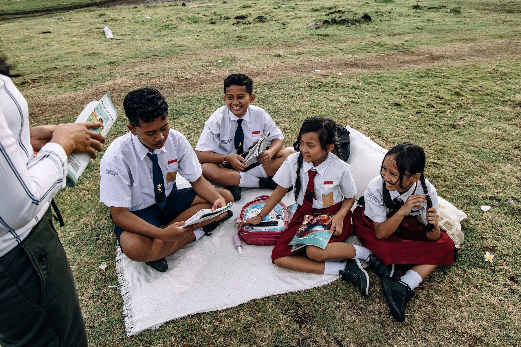 Siswa SD berseragam putih-merah membaca bersama di atas tikar di lapangan