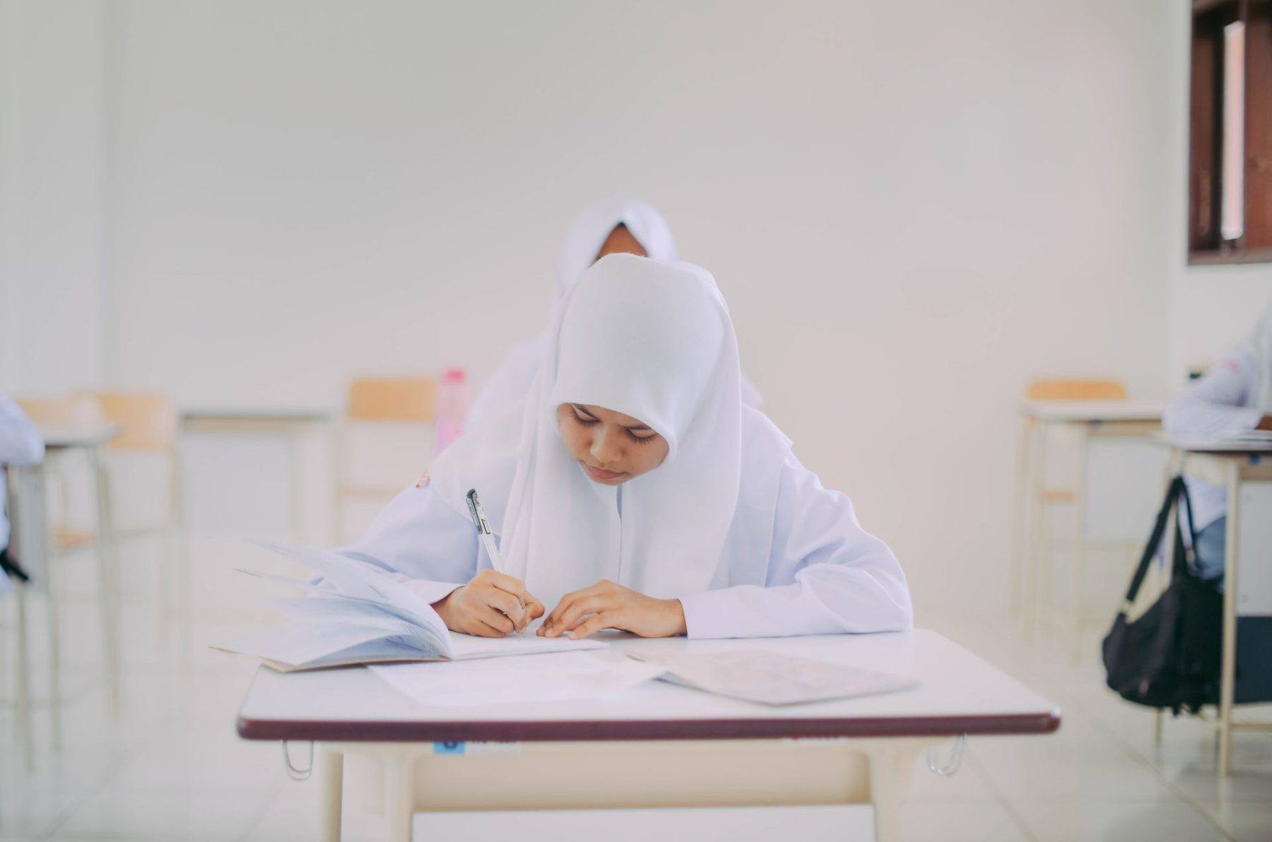 Siswi SMA berjilbab menulis dengan tekun di kelas